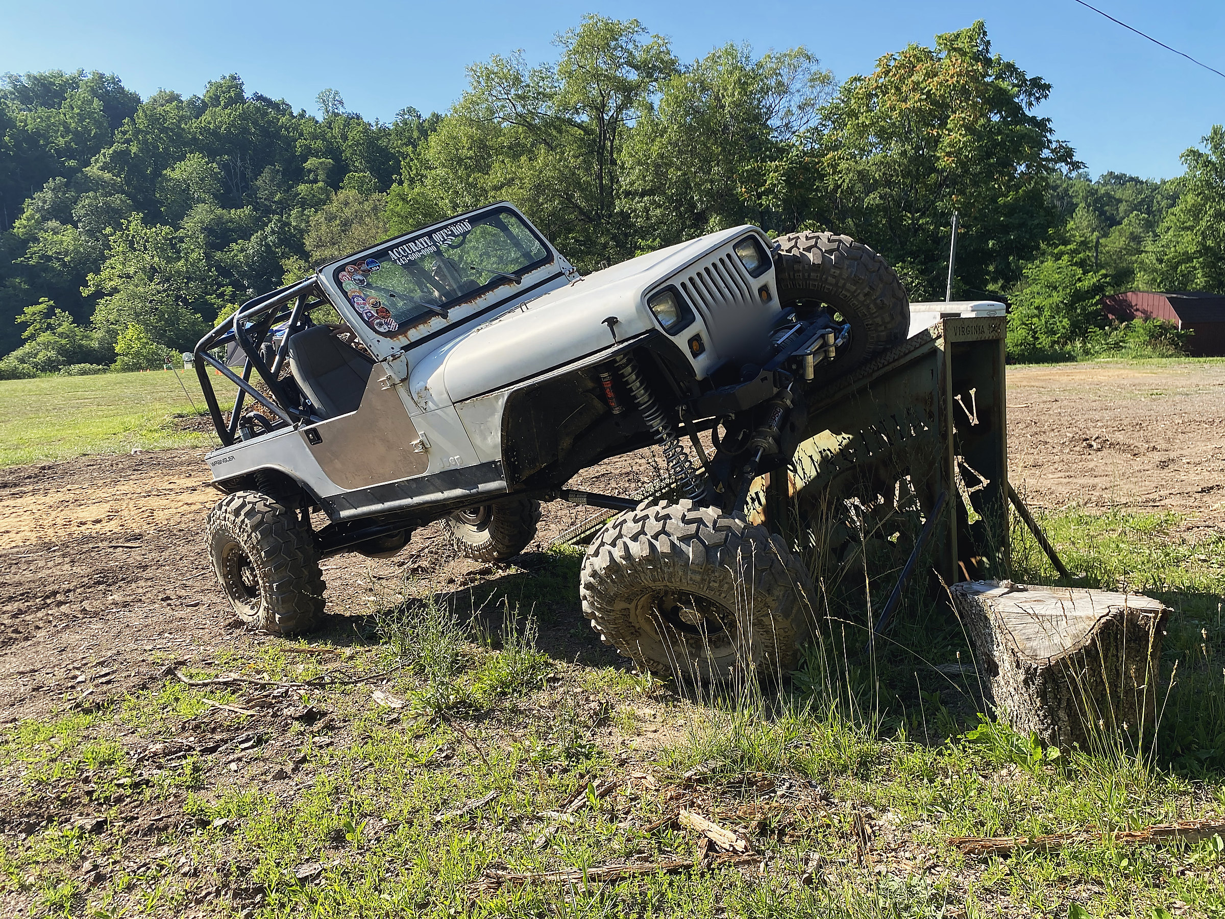 A lifted Jeep flexing its suspension on a steel ramp, with wooded hills behind it